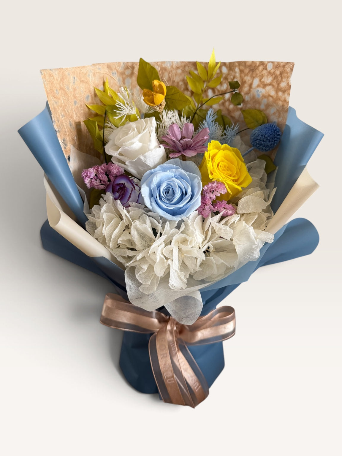 Bluebird Daydream preserved bouquet with blue, ivory, yellow, purple and pink flowers, blue and cream wrapping and champagne ribbon