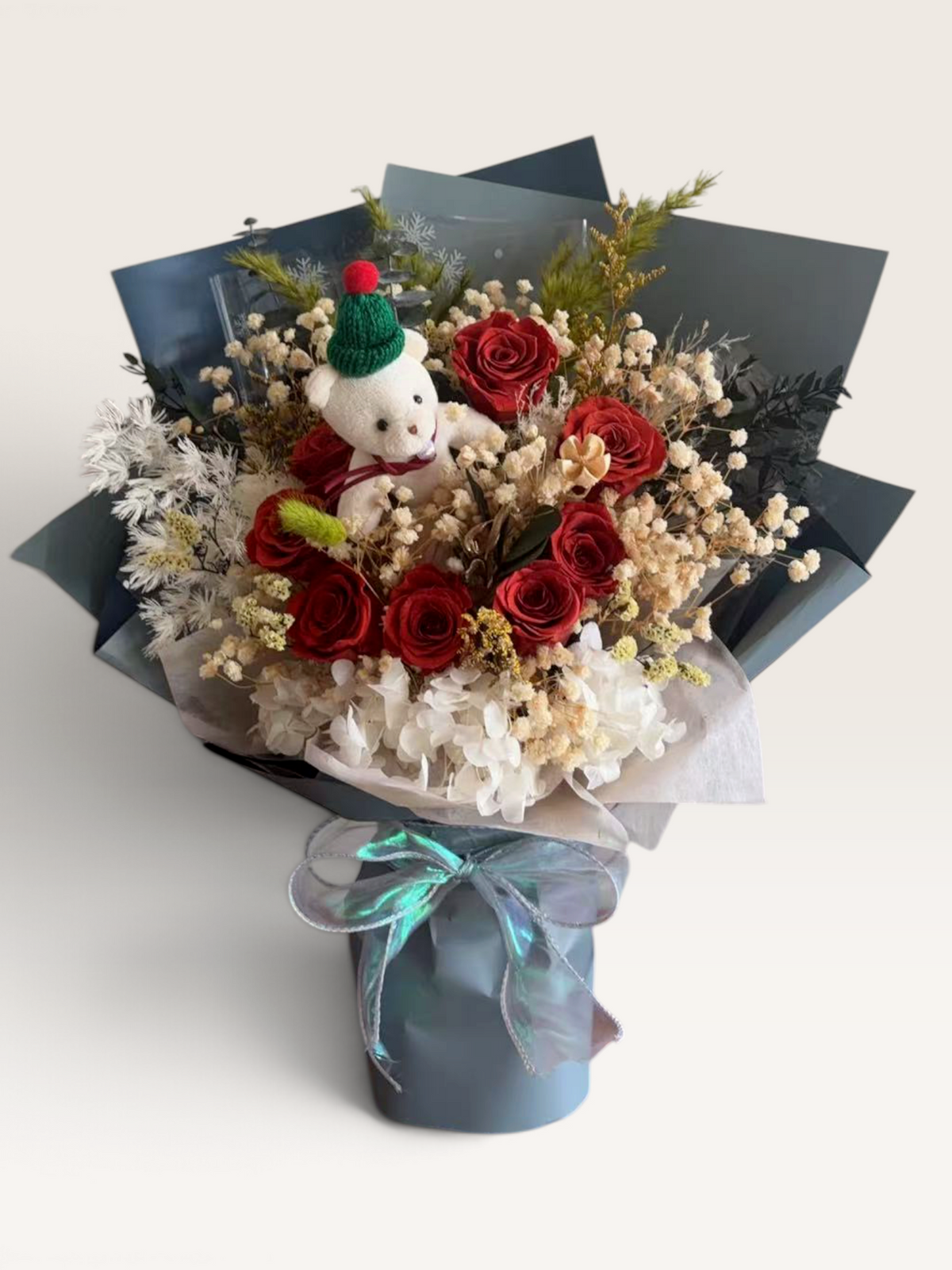 Christmas Bear Hugs bouquet with red preserved roses, ivory hydrangea and a white teddy bear wearing a green Christmas hat