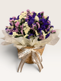 Forget Me Not floral decor with purple, lilac and ivory dried flowers in a woven basket with cream wrapping and ribbon