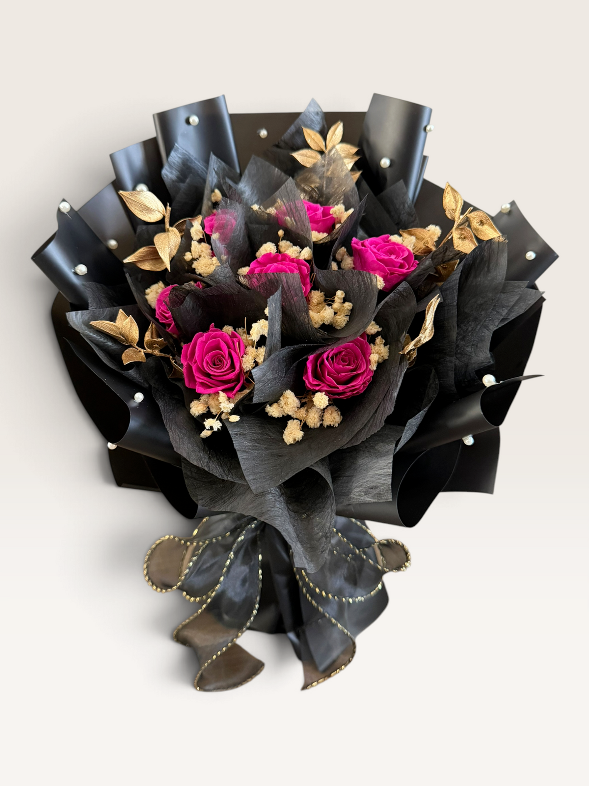 Fuchsia Majesty preserved rose bouquet in black wrapping with gold foliage and pearl accents